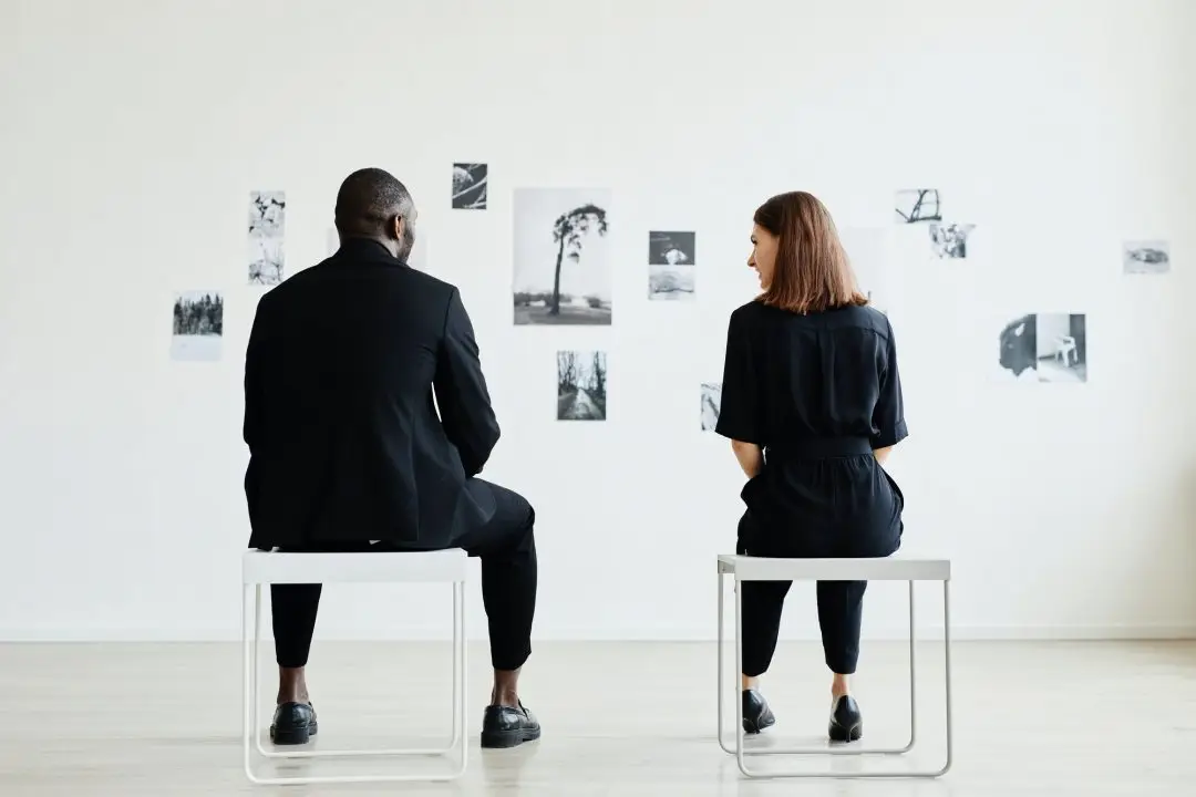 Two people sitting, observing wall photos.