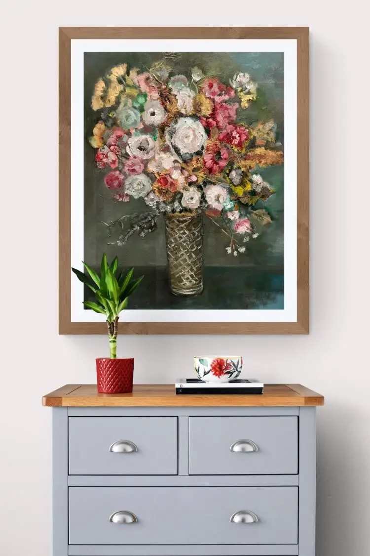 Floral painting above gray dresser with plant and cup.