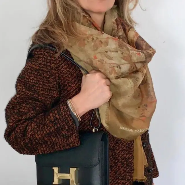 Woman in tweed coat holding black handbag with scarf.